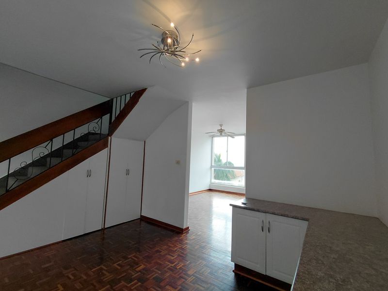 Open-plan living area featuring parquet flooring, under-stair storage, and a kitchen counter, leading to a bright space with a ceiling fan.