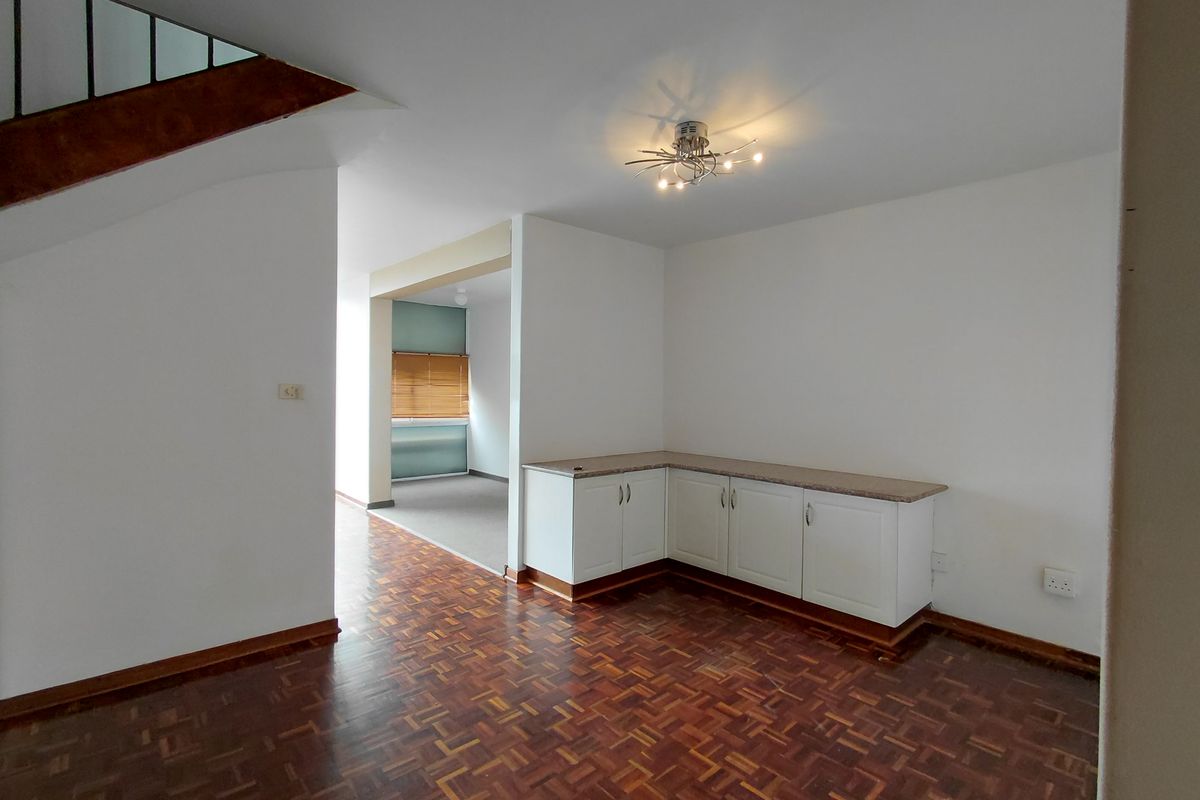 An open-plan living area featuring classic parquet flooring, built-in corner cabinetry with stone countertops, and a staircase leading to the upper level.