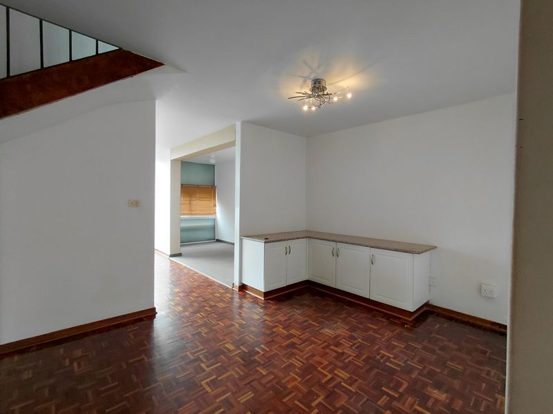 An open-plan living area featuring classic parquet flooring, built-in corner cabinetry with stone countertops, and a staircase leading to the upper level.