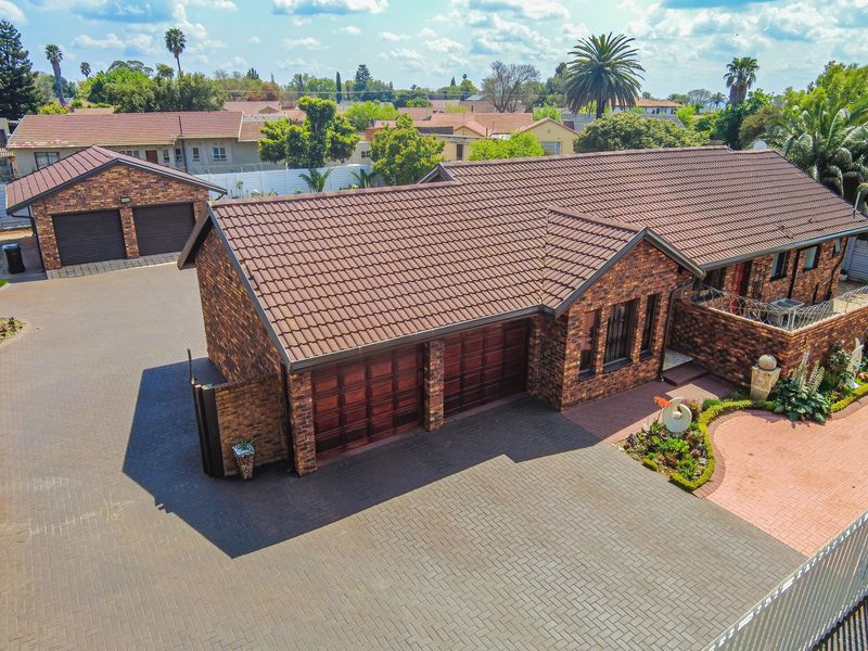 Aerial view of a well-maintained brick house featuring a tiled roof, double garage, extensive paved driveway, and established garden areas.