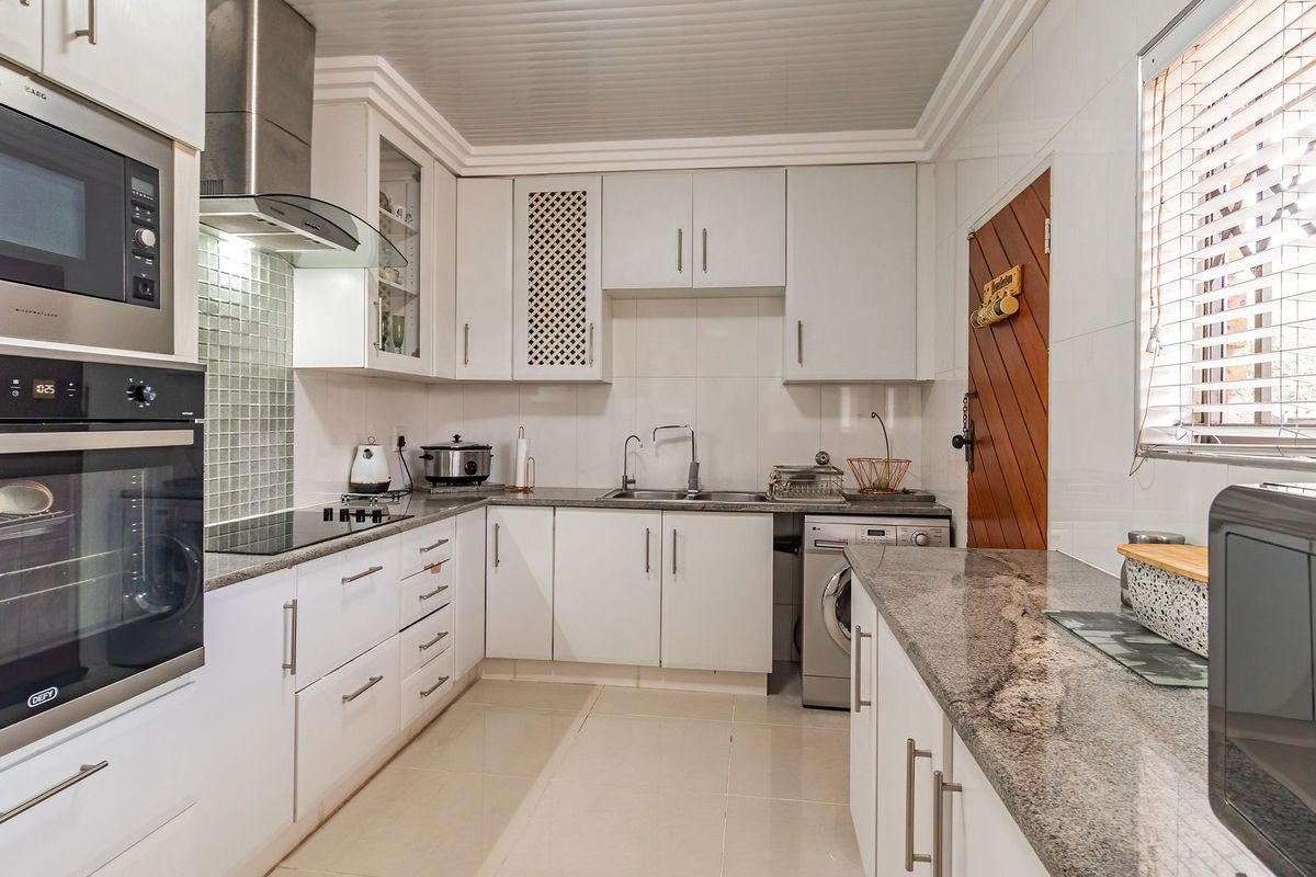 A well-maintained kitchen featuring white cabinetry, granite countertops, built-in appliances, and a tiled splashback, offering a clean and functional workspace.