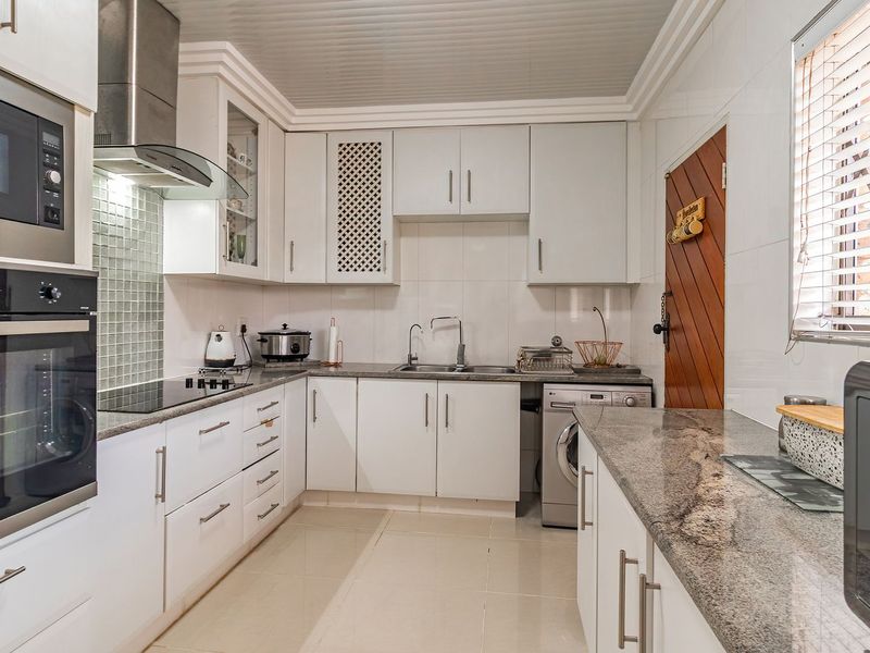 A well-maintained kitchen featuring white cabinetry, granite countertops, built-in appliances, and a tiled splashback, offering a clean and functional workspace.