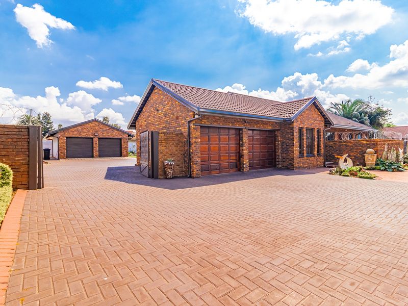 A well-maintained brick house featuring a spacious paved driveway, double garage, and secure perimeter fencing.
