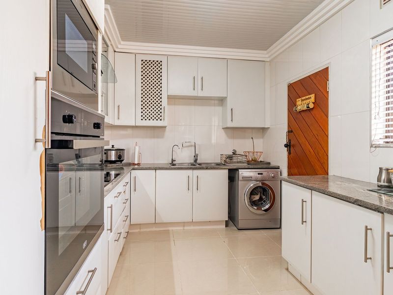 A functional kitchen featuring white cabinetry, granite countertops, built-in oven and microwave, and a tiled splashback with an integrated washing machine.