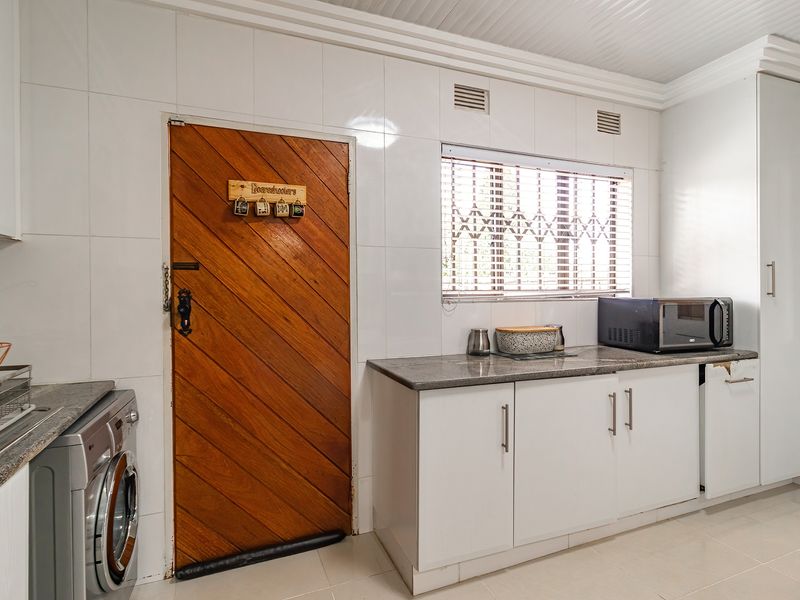 Functional laundry room featuring white built-in cabinetry, granite countertops, tiled walls, and direct access via a wooden door.