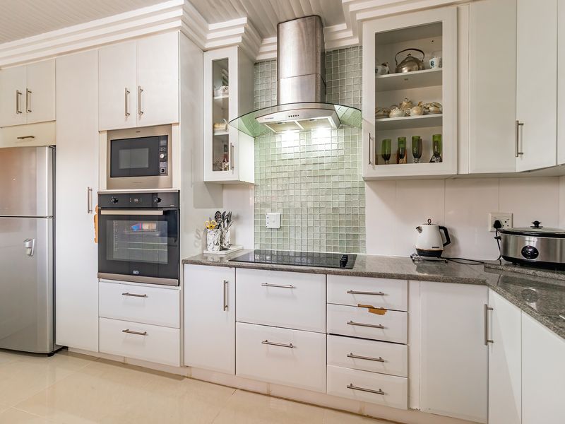 A functional kitchen featuring white cabinetry, granite countertops, a mosaic tile backsplash, and integrated appliances including an oven, microwave, and extractor fan.