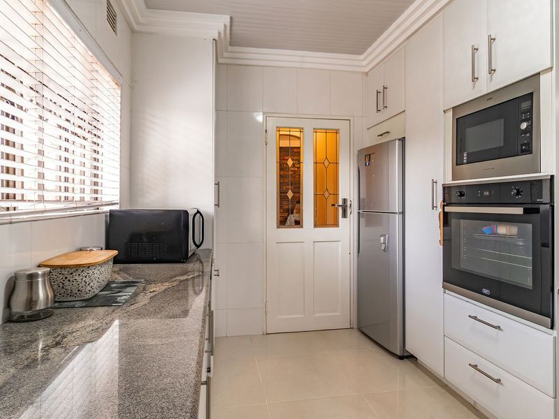 A well-maintained kitchen featuring granite countertops, built-in oven and microwave, tiled finishes, and a classic glass-panelled door.