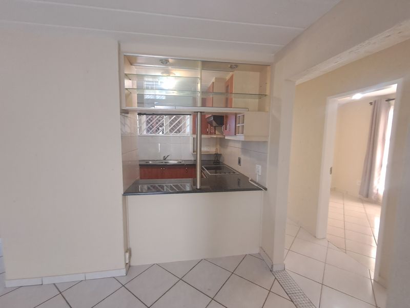 Compact kitchen featuring built-in cabinetry, granite countertops, an electric hob, and a convenient breakfast bar pass-through, finished with neutral tiled flooring.