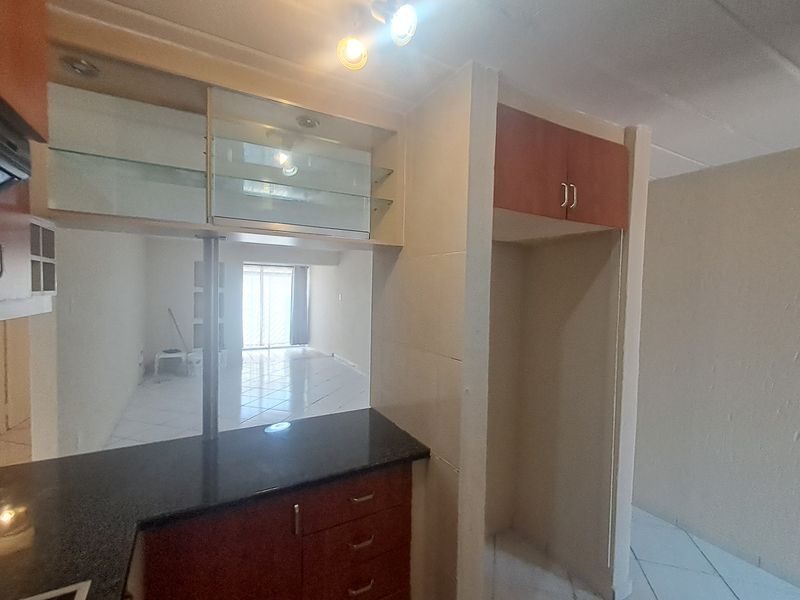 A functional kitchen area featuring granite countertops, built-in cabinetry with glass display sections, and a dedicated refrigerator alcove, opening into the living space.