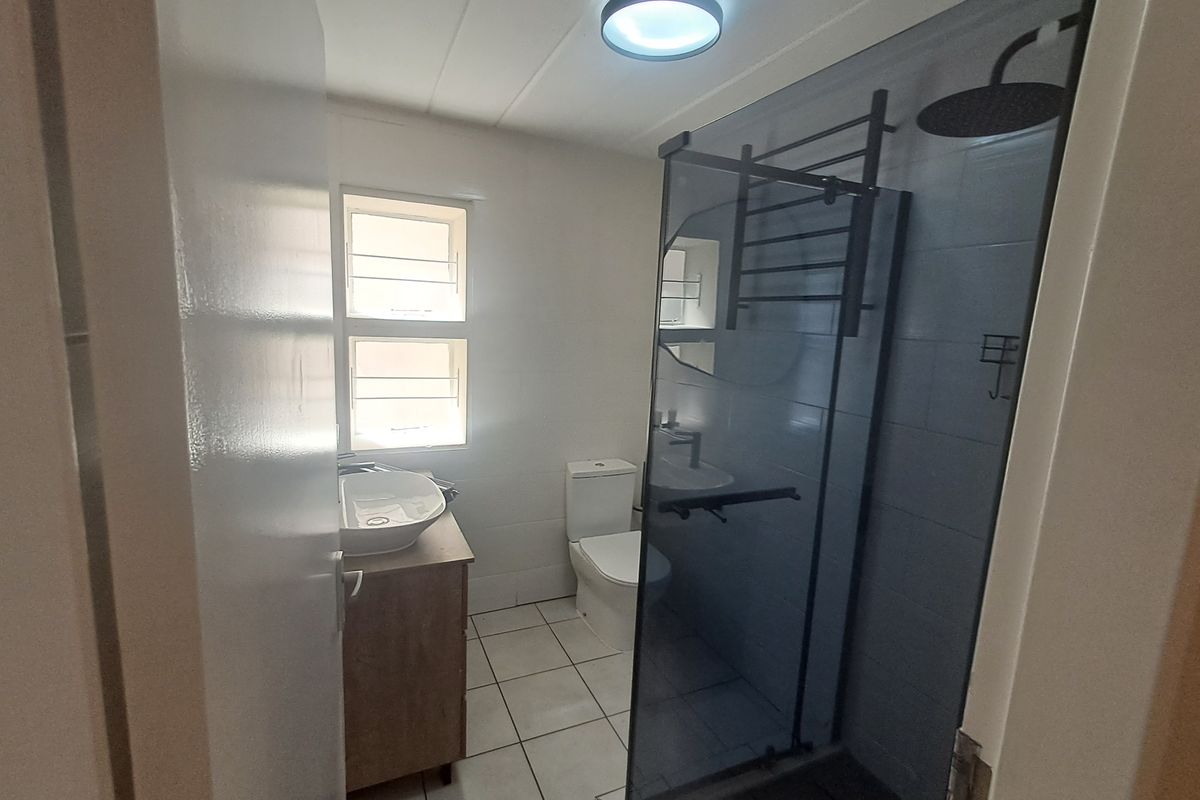 A clean, modern bathroom featuring a glass-enclosed shower with a rain shower head, a vanity with a vessel sink, and tiled flooring.