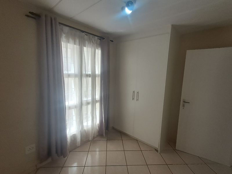 A bright, empty bedroom featuring tiled flooring, a built-in wardrobe, and a window fitted with security bars.