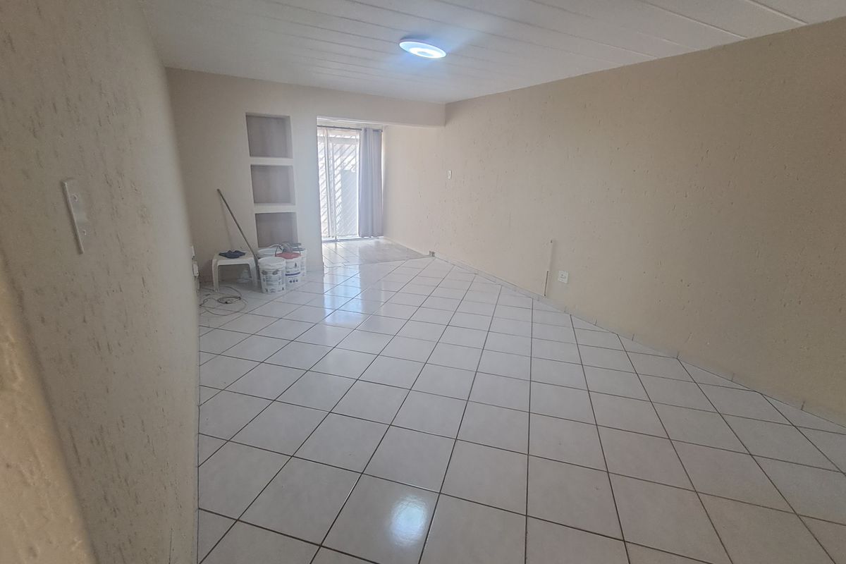 An empty, open-plan living area featuring neutral tiled flooring, built-in wall niches, and a security gate leading to an outdoor space.