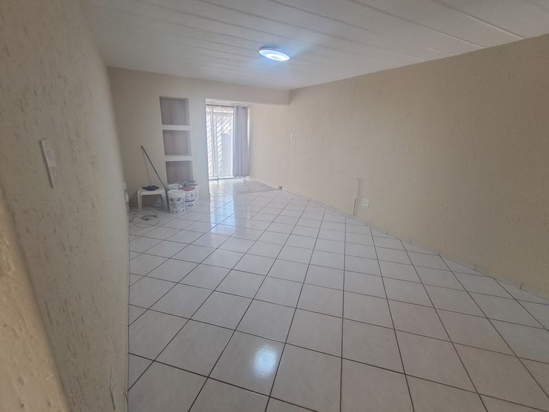 An empty, open-plan living area featuring neutral tiled flooring, built-in wall niches, and a security gate leading to an outdoor space.