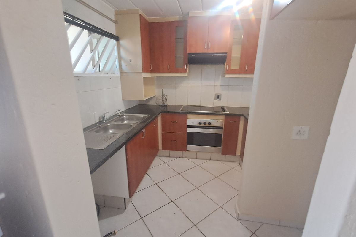 A functional kitchen featuring built-in cabinetry, a double sink, electric hob, and oven, with tiled flooring and splashbacks throughout.