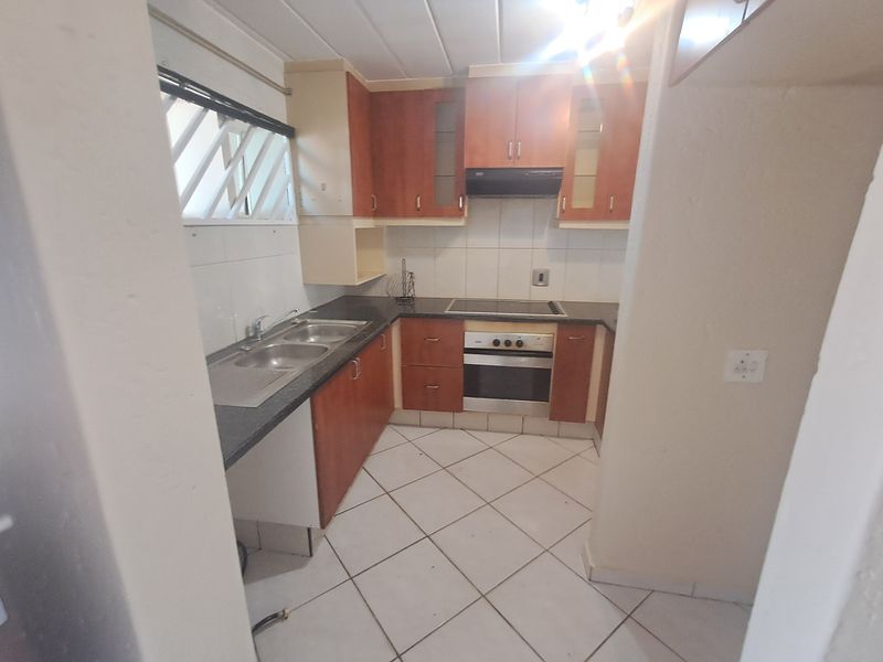 A functional kitchen featuring built-in cabinetry, a double sink, electric hob, and oven, with tiled flooring and splashbacks throughout.