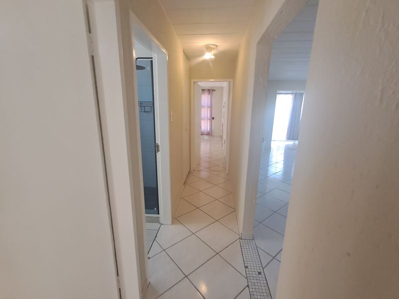 A functional hallway connecting multiple rooms, featuring neutral ceramic floor tiles and basic lighting fixtures throughout the space.