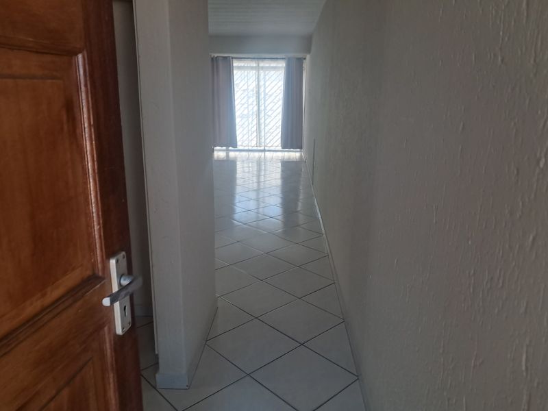 A vacant hallway with tiled flooring leading towards a sliding glass door with a security gate.