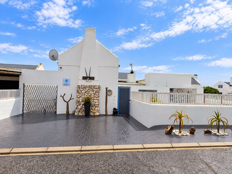 Front elevation of a white-painted house featuring a stone-clad chimney, paved driveway, and secure gated entrance.