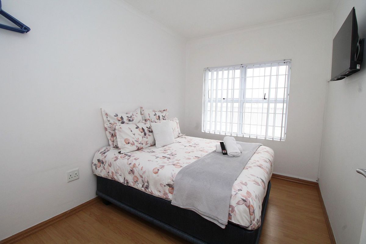 A functional bedroom featuring laminate flooring, a window with security bars, and a wall-mounted television.
