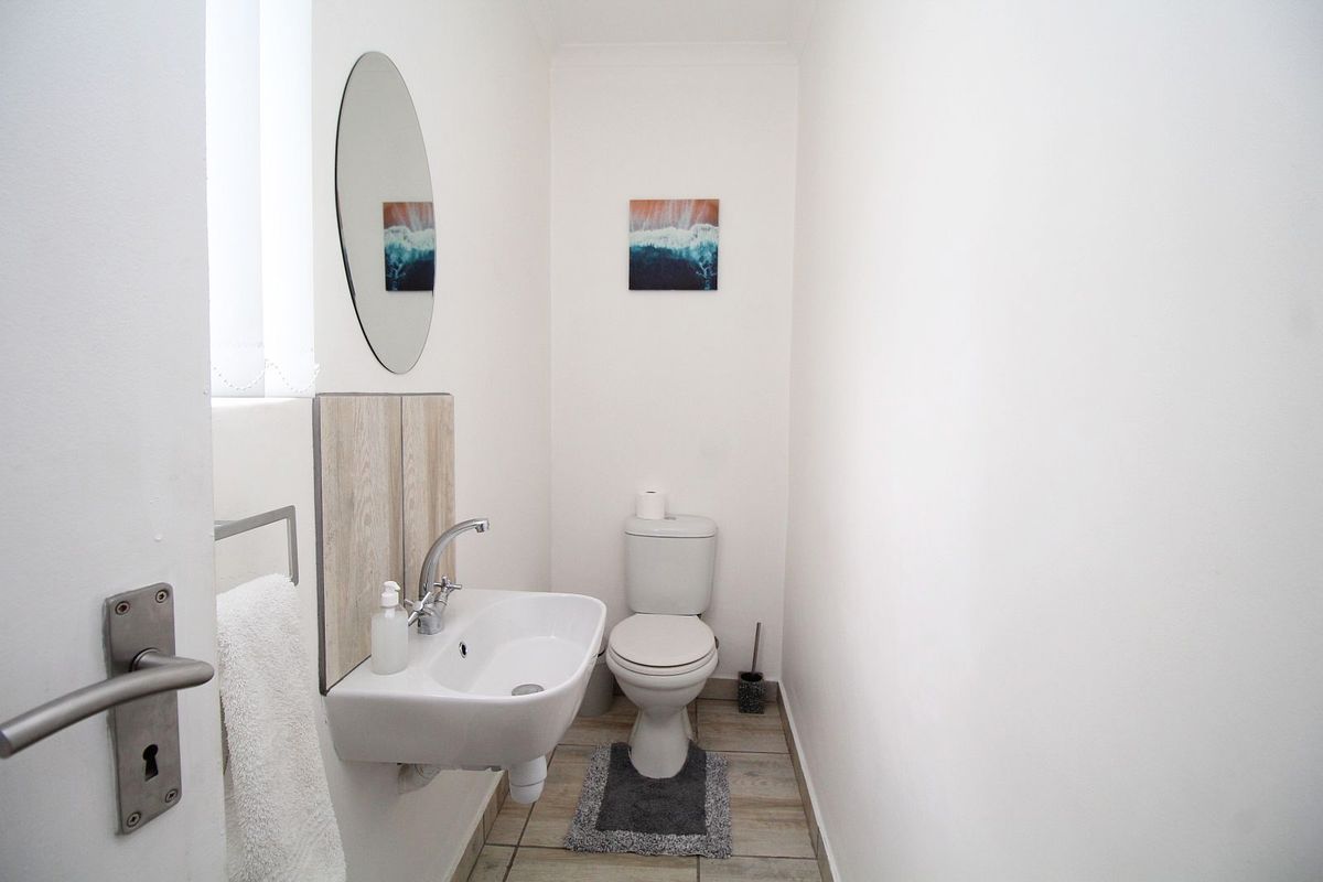 A clean and functional guest bathroom featuring a wall-mounted basin, modern mixer tap, and standard toilet with neutral tiled flooring.