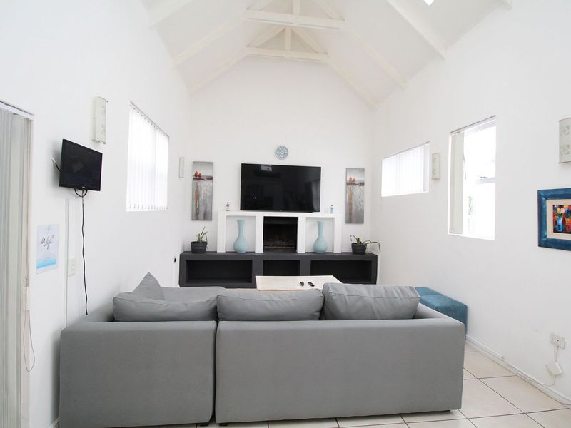 A bright living room featuring a high vaulted ceiling, tiled flooring, and a built-in media console with integrated shelving.