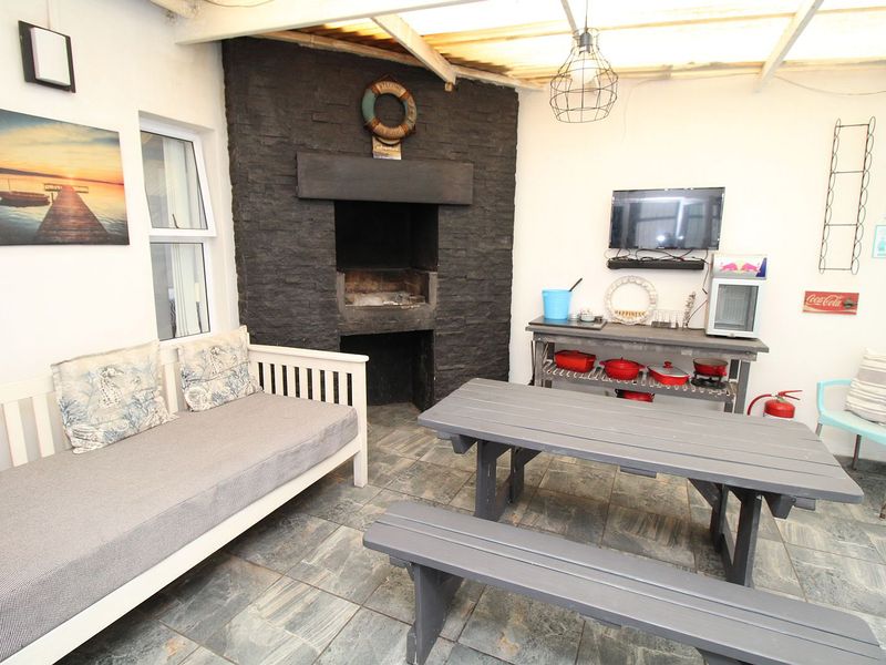 Covered patio area featuring a built-in braai with stone cladding, tiled flooring, and a translucent roof, ideal for outdoor entertaining.