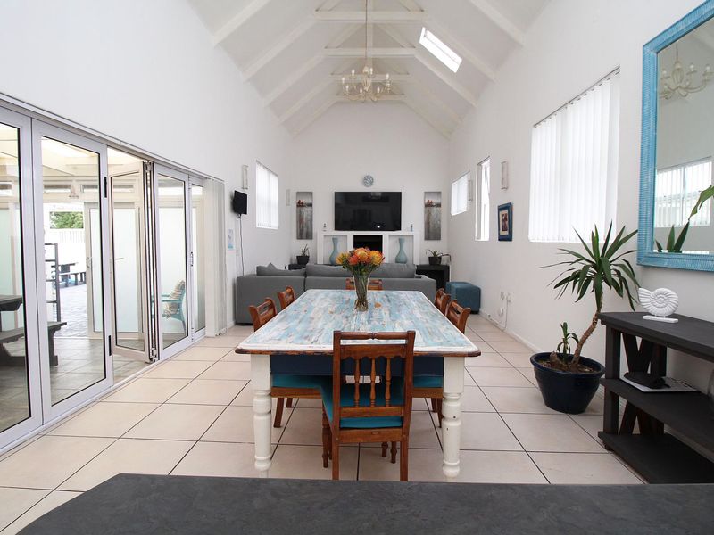 Spacious open-plan living and dining area featuring a high vaulted ceiling, skylights, tiled flooring, and large bi-fold doors opening to the patio.