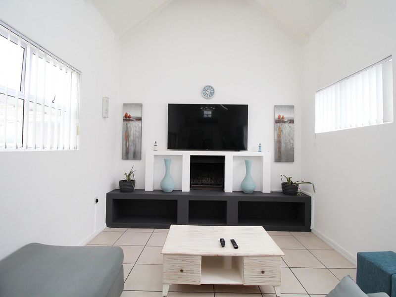 A bright living room featuring a vaulted ceiling, tiled flooring, and a custom built-in media console with an integrated fireplace.