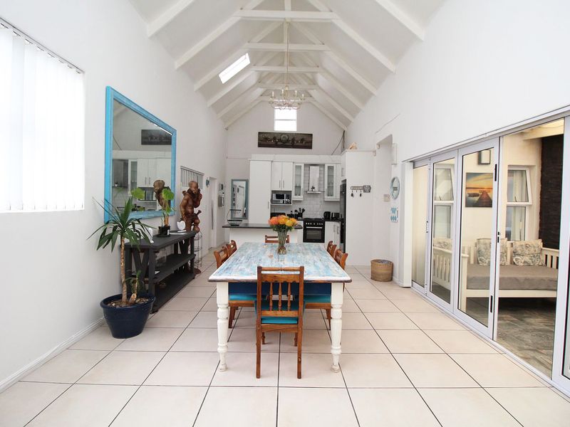 Spacious open-plan living and dining area featuring a high vaulted ceiling, skylights, tiled floors, and direct access to the patio through sliding glass doors.