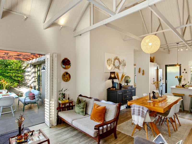 Bright open-plan living and dining area featuring vaulted ceilings with exposed trusses, seamless flow to an outdoor patio, and a modern kitchen island.