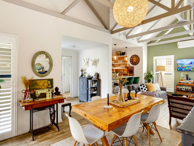 Spacious open-plan living and dining area featuring vaulted ceilings with exposed trusses, laminate flooring, and plantation shutters, creating a bright and airy atmosphere.