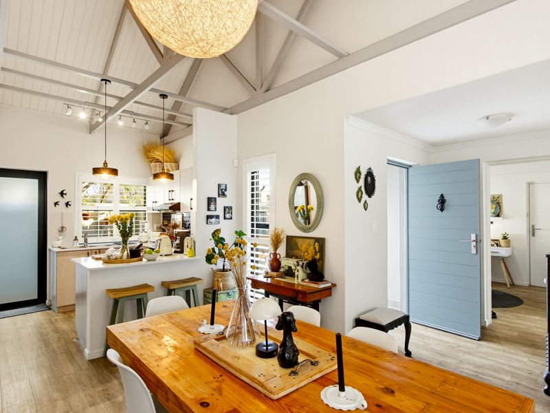 Bright open-plan living and dining area featuring a vaulted ceiling with exposed rafters, a modern kitchen island, and light wood-look flooring.