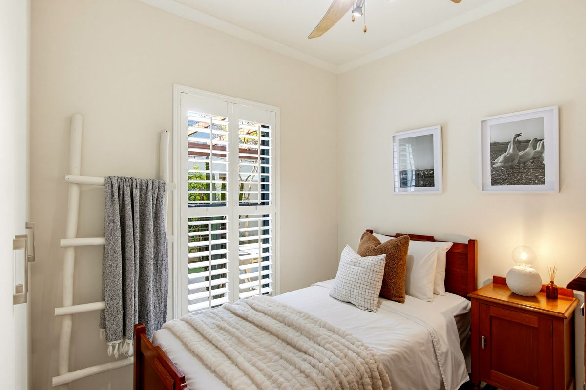 A well-maintained bedroom featuring plantation shutters, a ceiling fan, and a built-in wardrobe, offering a bright and comfortable living space.