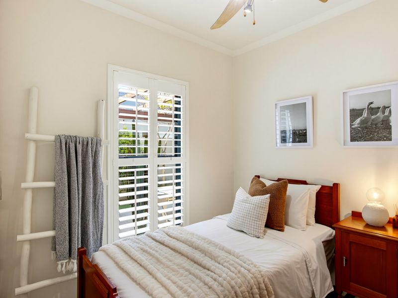 A well-maintained bedroom featuring plantation shutters, a ceiling fan, and a built-in wardrobe, offering a bright and comfortable living space.