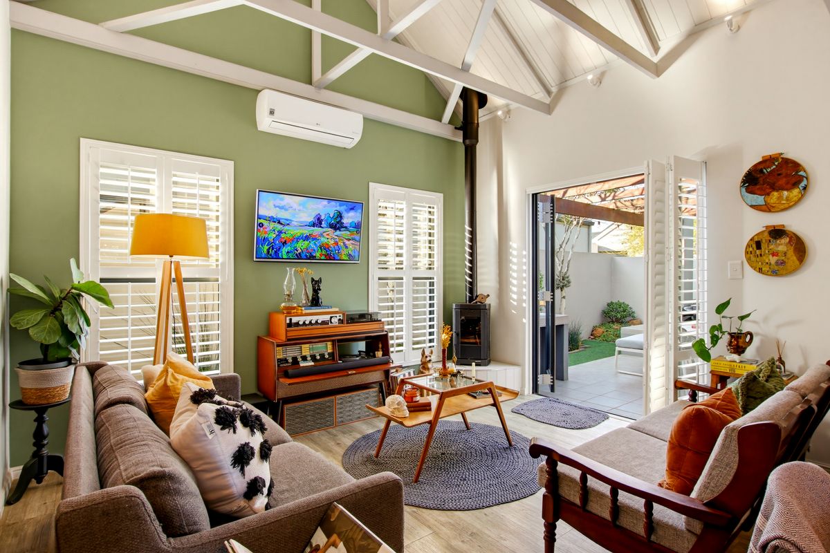 A bright living room featuring a vaulted ceiling with exposed rafters, a wood-burning stove, and bi-fold doors opening to an outdoor patio area.