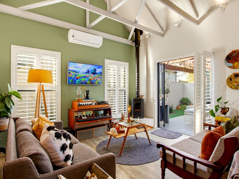 A bright living room featuring a vaulted ceiling with exposed rafters, a wood-burning stove, and bi-fold doors opening to an outdoor patio area.
