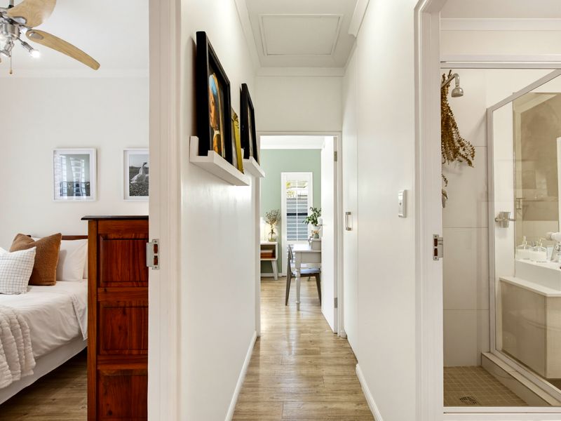 A bright hallway connecting a bedroom and bathroom, featuring light wood-look flooring, clean white walls, and access to a secondary room.