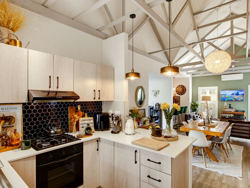 Modern open-plan kitchen and dining area featuring light wood cabinetry, stone countertops, exposed vaulted rafters, and contemporary pendant lighting.