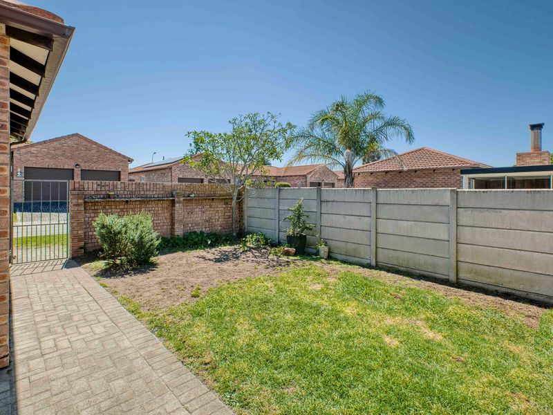 A private rear garden featuring a paved walkway, a combination of brick and precast concrete boundary walls, and a small lawn area.