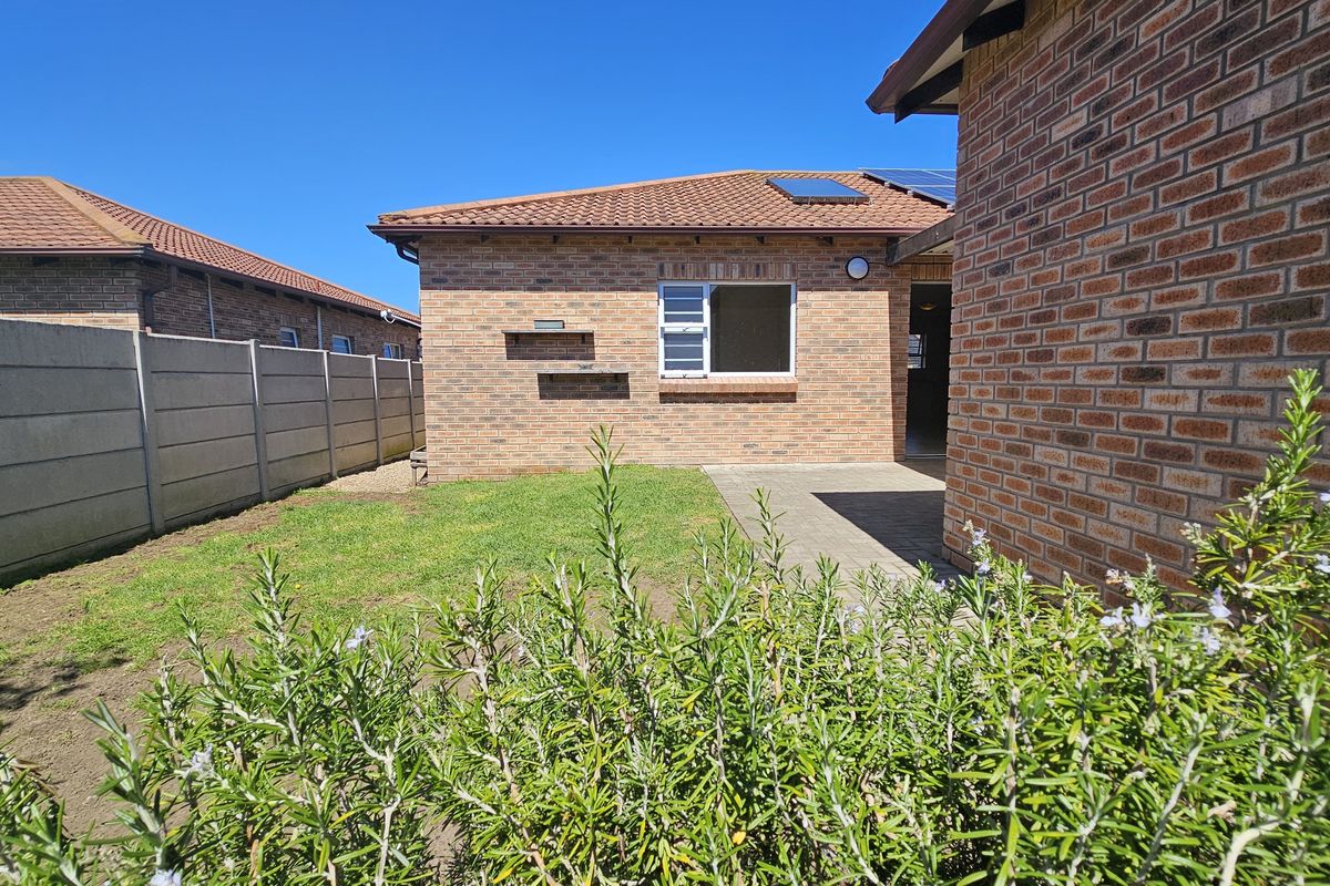 Rear view of the property featuring a face brick exterior, tiled roof, paved patio area, and a private garden enclosed by precast concrete walls.