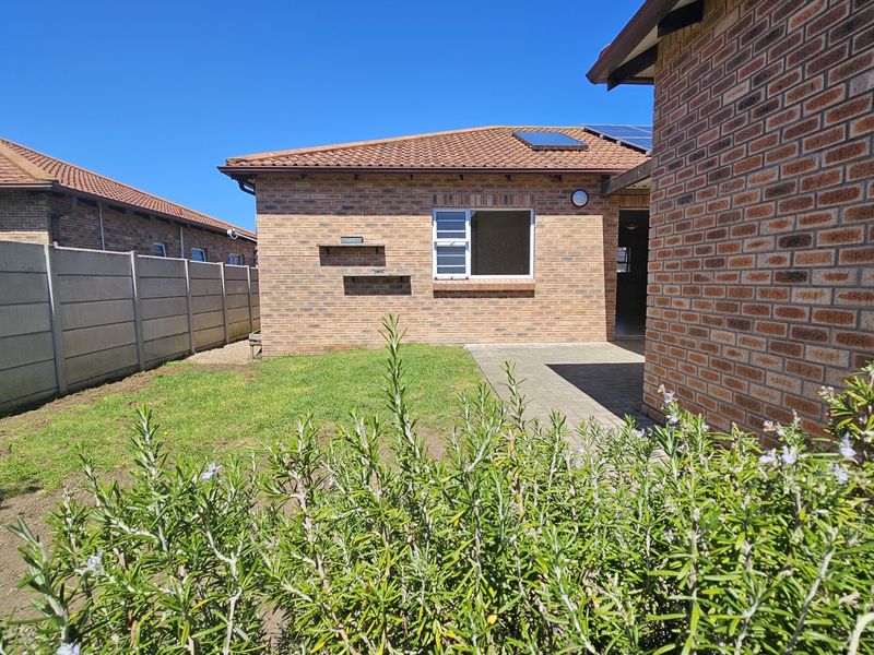 Rear view of the property featuring a face brick exterior, tiled roof, paved patio area, and a private garden enclosed by precast concrete walls.