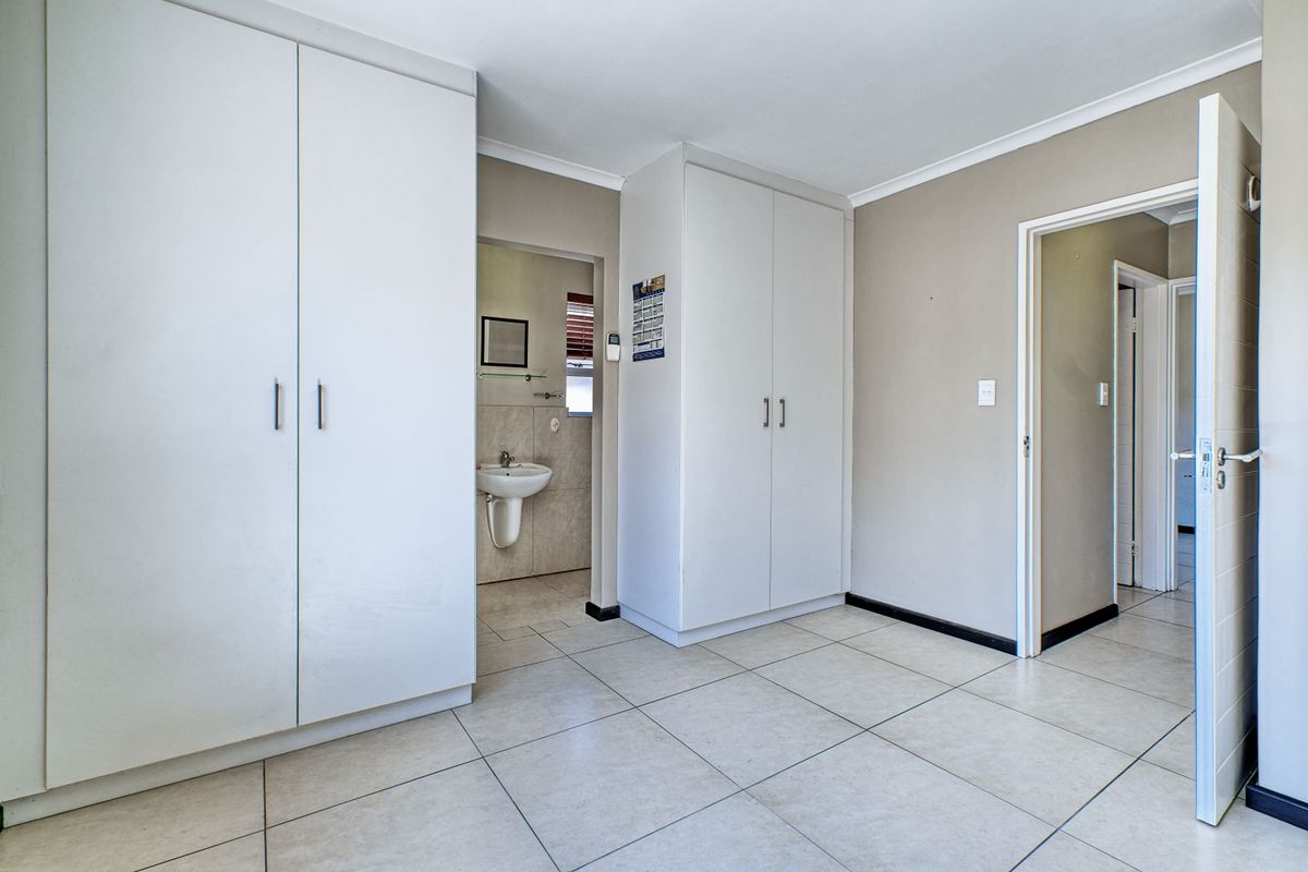 A clean, empty bedroom featuring neutral tiled flooring, ample built-in cupboard storage, and direct access to an en-suite bathroom.