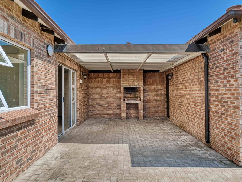 A covered outdoor patio featuring a built-in brick braai, paved flooring, and direct access to the home via sliding glass doors.
