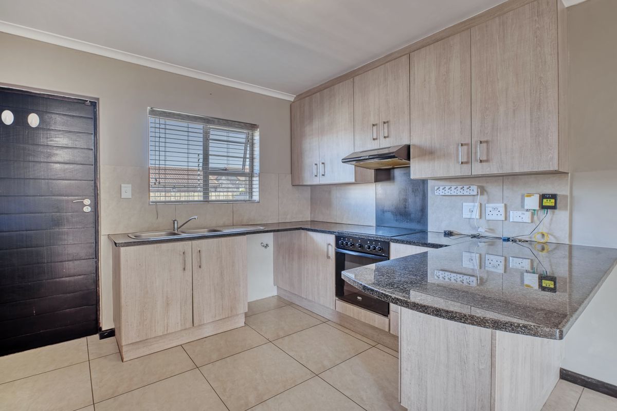 A functional kitchen featuring light wood-finish cabinetry, granite countertops, a built-in oven with extractor fan, and tiled flooring.