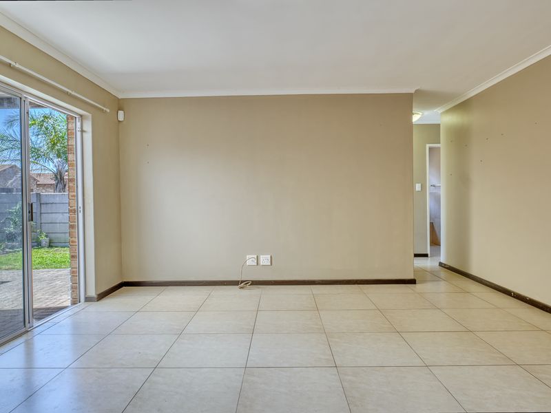 An empty, neutrally painted living room featuring ceramic floor tiles, coved ceilings, and a sliding glass door providing access to the rear garden.