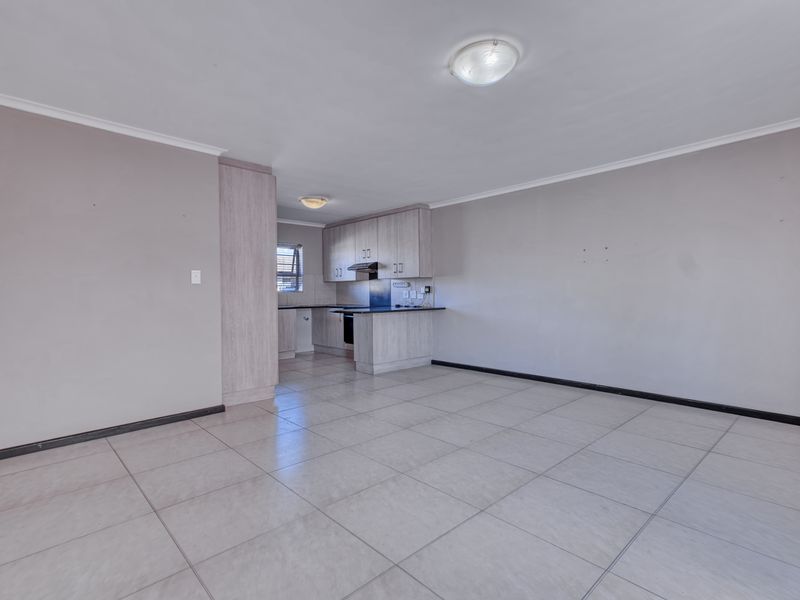 Spacious open-plan living area featuring neutral tiled flooring and a compact kitchen with built-in cabinetry and an extractor fan.