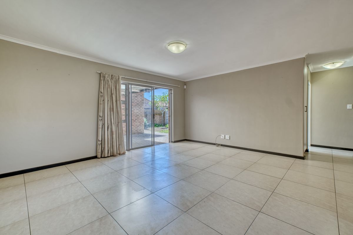 A spacious, empty living room featuring neutral tiled flooring and a sliding glass door providing access to the rear patio area.
