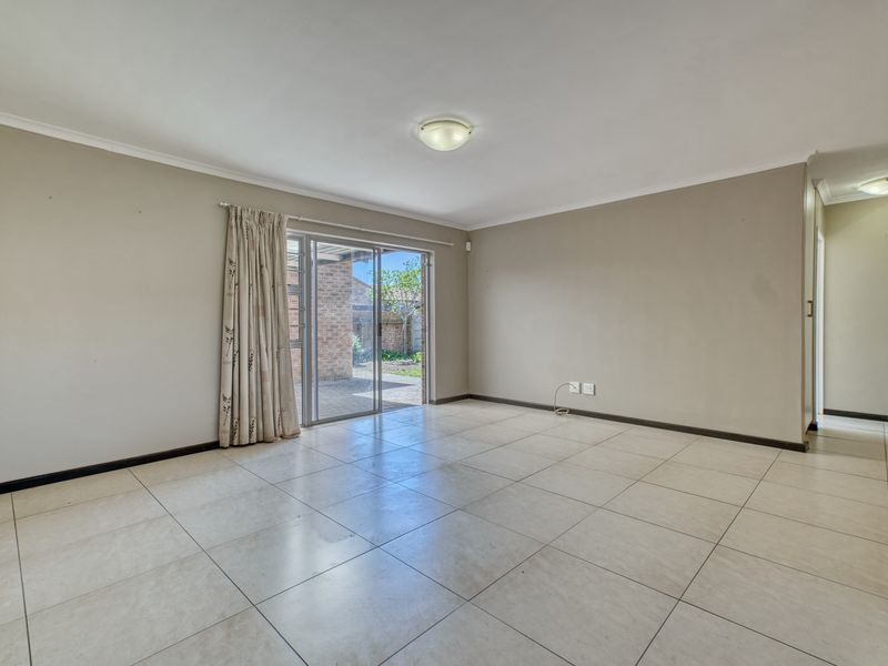 A spacious, empty living room featuring neutral tiled flooring and a sliding glass door providing access to the rear patio area.