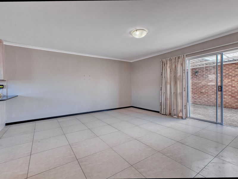 An empty open-plan living area featuring tiled flooring, neutral walls, and a sliding glass door providing access to an outdoor patio space.