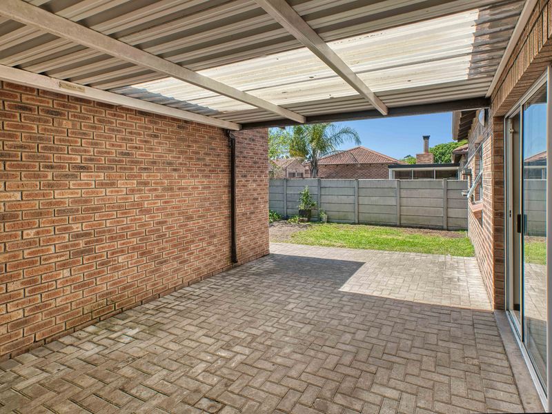 A covered outdoor patio area featuring brick walls, paved flooring, and direct access to the rear garden through sliding glass doors.